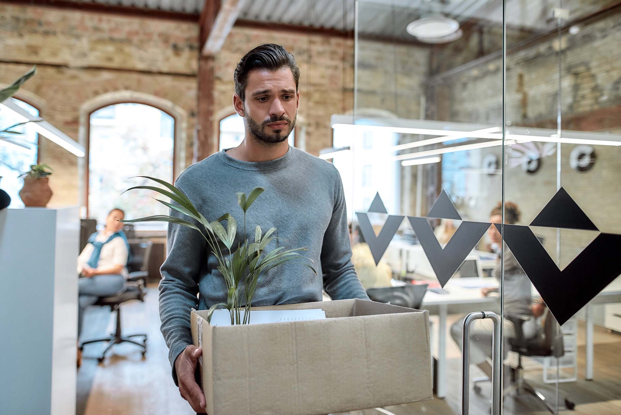 A sad looking employee leaving an office with a box full of his beings